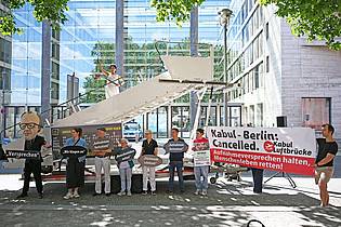 Michael Brandt/dpa | Aktivsten stehen während einer symbolischen Protestaktion am Weltflüchtlingstag zur Unterstützung mehrerer Klagen von Afghanen gegen die Bundesregierung vor dem Auswärtigen Amt.