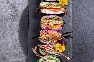 Alex Neumayer/Christian Verlag/dpa-tmn | Wer sich für die Vorbereitung etwas mehr Zeit nimmt, kann Sushi-Sandwiches mitbringen - ein hier noch mit essbaren Blüten verzierter Hingucker.