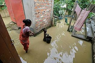 Uncredited/AP/dpa | Eine Frau versucht in der überfluteten Umgebung ihres Hauses, Wasser zu sammeln. 