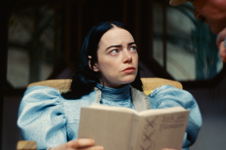 Emma Stone im Film "Poor Things" mit einem Buch, schaut zur Seite 
