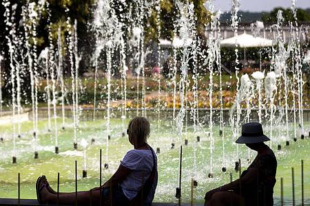 Michael Reichel/dpa | Zwei Frauen sitzen an einem Springbrunnen im egapark in Erfurt in Thüringen.