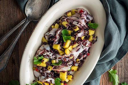 Valerie Hammacher/ars vivendi/dpa-tmn | Wenn es mal etwas ganz Exotisches sein soll: Dieser schwarze Reissalat mit Mango und Oktopus sticht auf einer Mitbringfeier sicher heraus.