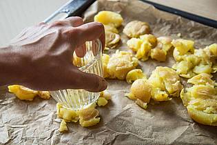 Christin Klose/dpa-tmn | Die gekochten Kartoffeln kommen auf ein Backblech und werden mit einem Glas zerdrückt. Mit Olivenöl bepinseln und Salzflocken bestreuen, dann 40 bis 45 Minuten knusprig backen.