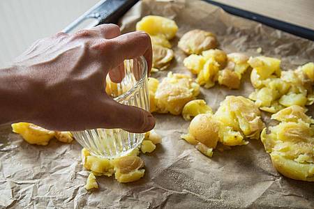 Christin Klose/dpa-tmn | Die gekochten Kartoffeln kommen auf ein Backblech und werden mit einem Glas zerdrückt. Mit Olivenöl bepinseln und Salzflocken bestreuen, dann 40 bis 45 Minuten knusprig backen.