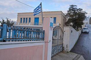 Petros Giannakouris/AP/dpa | Eine griechische Flagge weht vor einer geschlossenen Grundschule. (Archivbild)