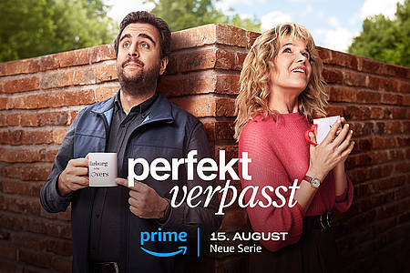 Anke Engelke und Bastian Pastewka lehnen als Hauptcharaktere von Perfekt Verpasst auf Prime Video an einer Mauer.