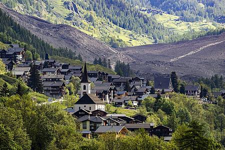 Jean-Christophe Bott/KEYSTONE/dpa | Das Dorf Kippel wurde verschont, dahinter ist die Wüste aus Eis, Schlamm und Fels zu sehen.