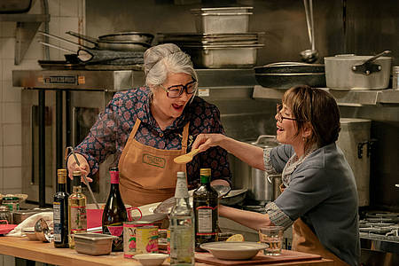 Zwei italienische Seniorinnen in der Küche lachen sich beim Kochen an.