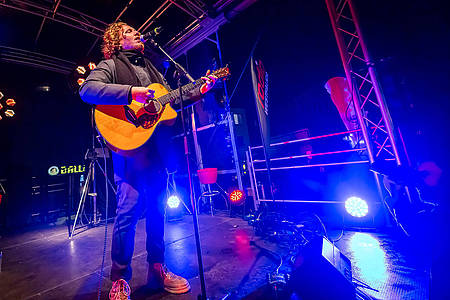 Michael Schulte steht mit seiner Gitarre auf einer Bühne und singt in ein Mikrofon