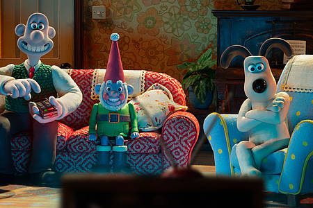 Die Knetfiguren Wallace und Gromit sitzen samt Gartenzwerg auf dem Sofa und schauen Fernsehen.