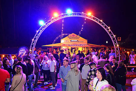 Tanz in den Mai im Kohlpott, viele Menschen im lilanen Scheinwerferlicht, Bier-Station im Hintergrund